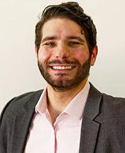 headshot photo of Dr. Kevin Duquette smiling with brown hair, mustache and beard wearing a gray blazer over a pink button down shirt