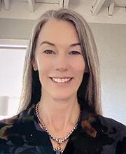 headshot photo of Christy Lyons Graham smiling with long straight gray hair wearing dark colored floral v-neck collared top