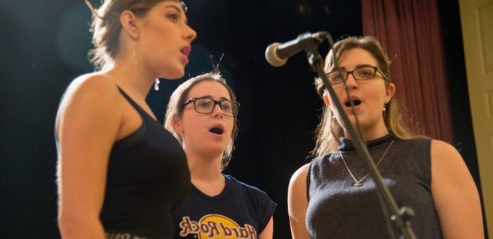 Three student singers standing around a microphone singing.